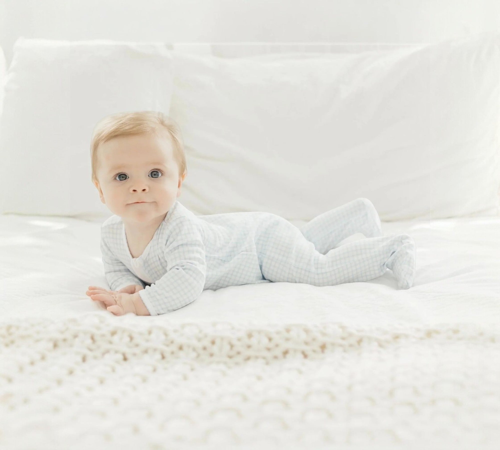 Baby lying on a white bed wearing a light gray onesie.