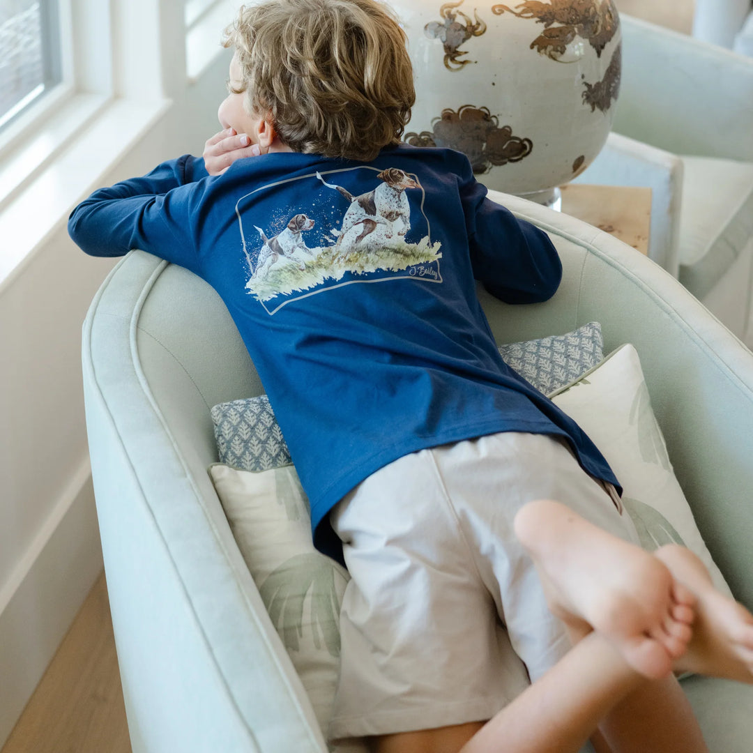 Child sitting on a white chair wearing a blue shirt with a dog graphic, in a bright room.