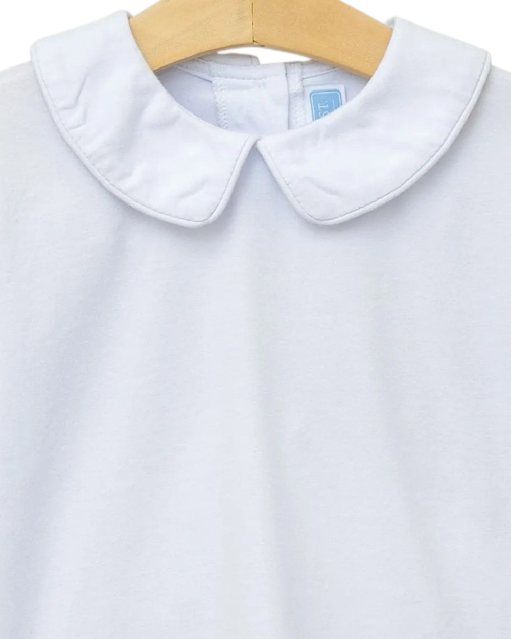 A close-up of a white long-sleeve top with a wide flat collar, hanging on a light wood hanger against a white background, that store