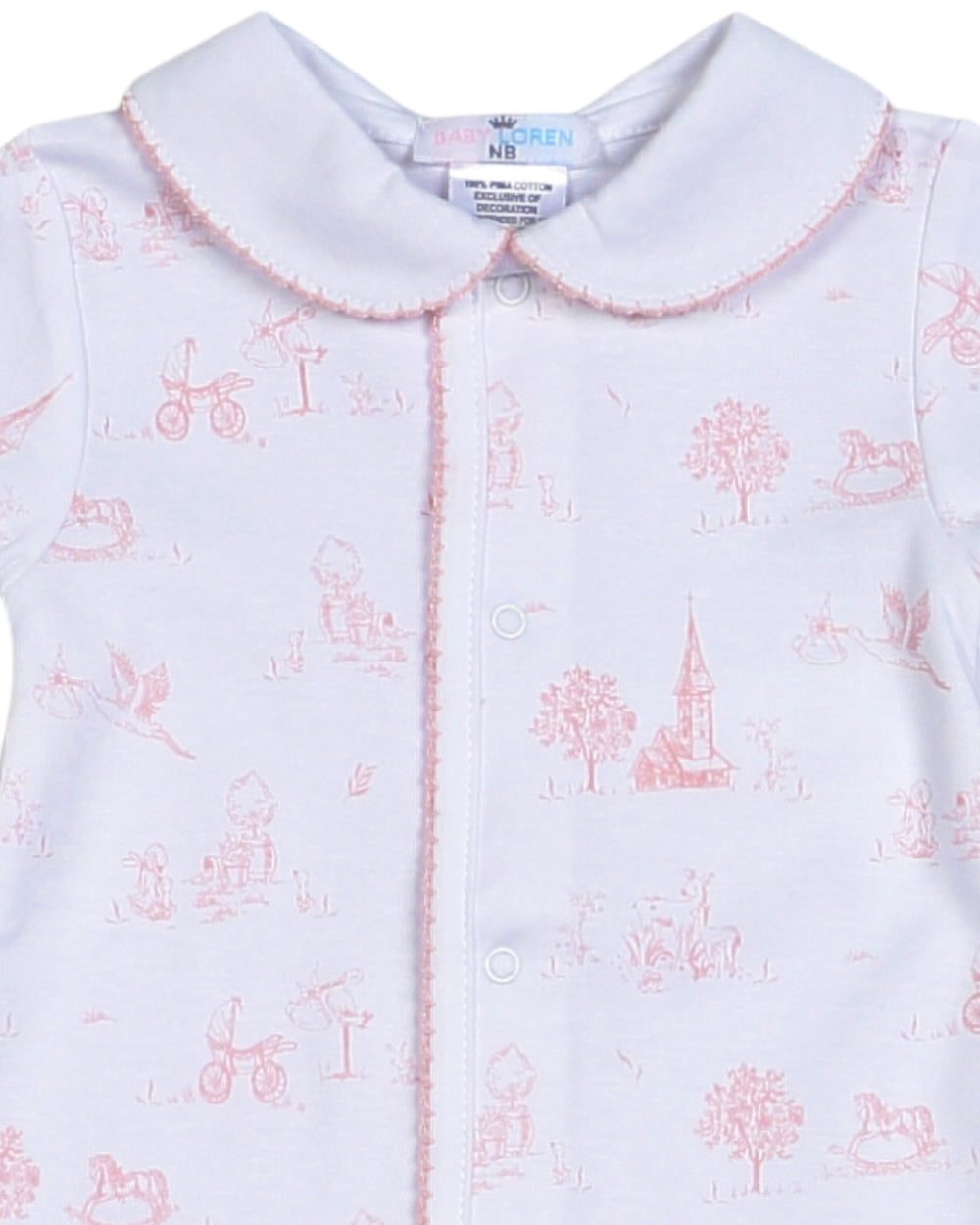 A close-up of a baby garment featuring a white base with a delicate pink toile-style print of classic toys, trees, and a church steeple, finished with a pink scalloped collar, that store