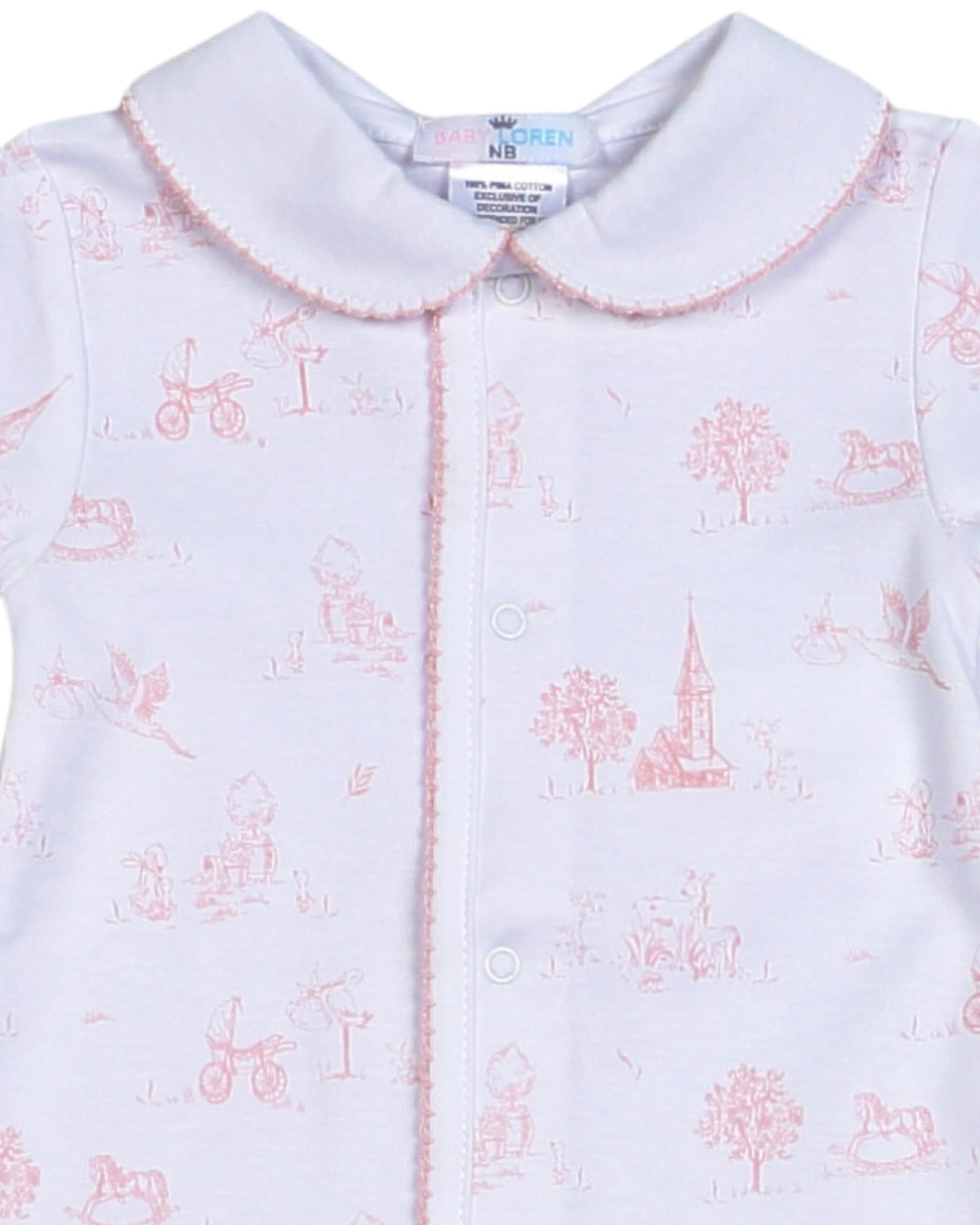 A close-up of a baby garment featuring a white base with a delicate pink toile-style print of classic toys, trees, and a church steeple, finished with a pink scalloped collar, that store