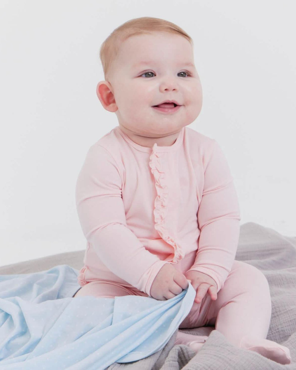 Baby in a pink outfit sitting on a light blue blanket with a white background