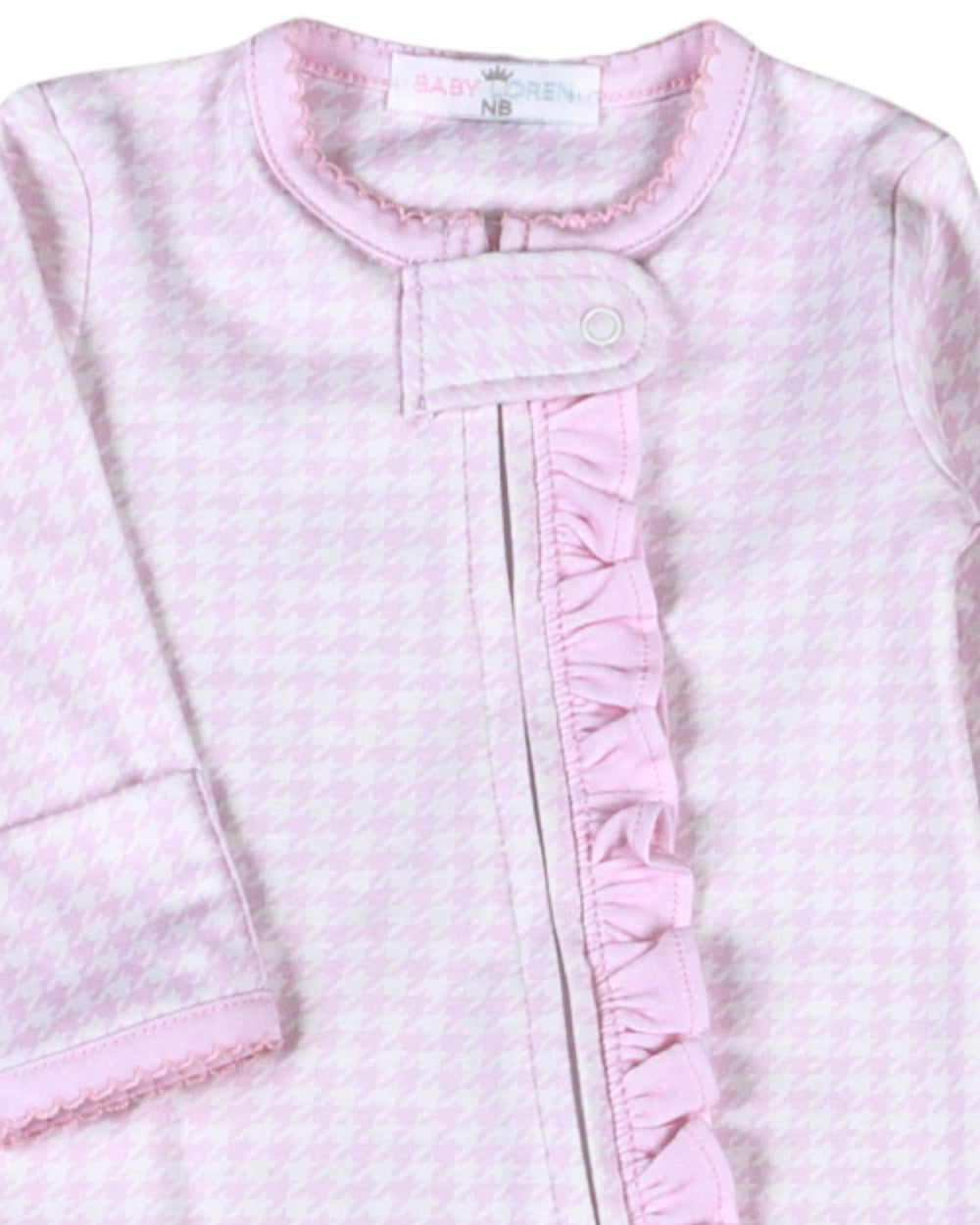 A close-up of a baby sleep sack or long-sleeve sleeper in light pink and white with a fine houndstooth pattern, featuring a ruffled trim down the front and a snap-button closure, that store