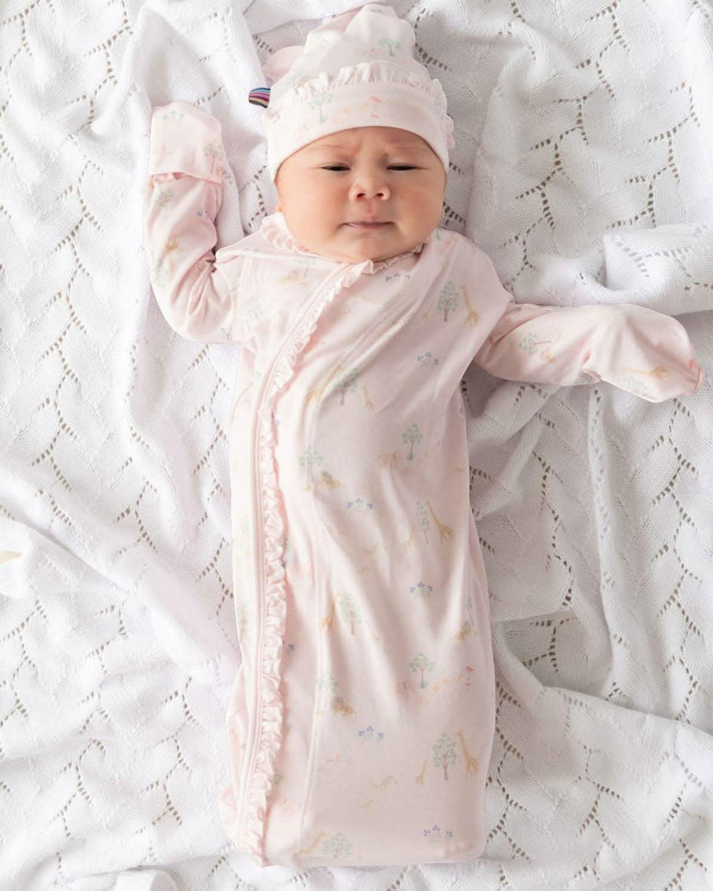 Baby wrapped in a pink swaddle with a matching hat on a white textured blanket