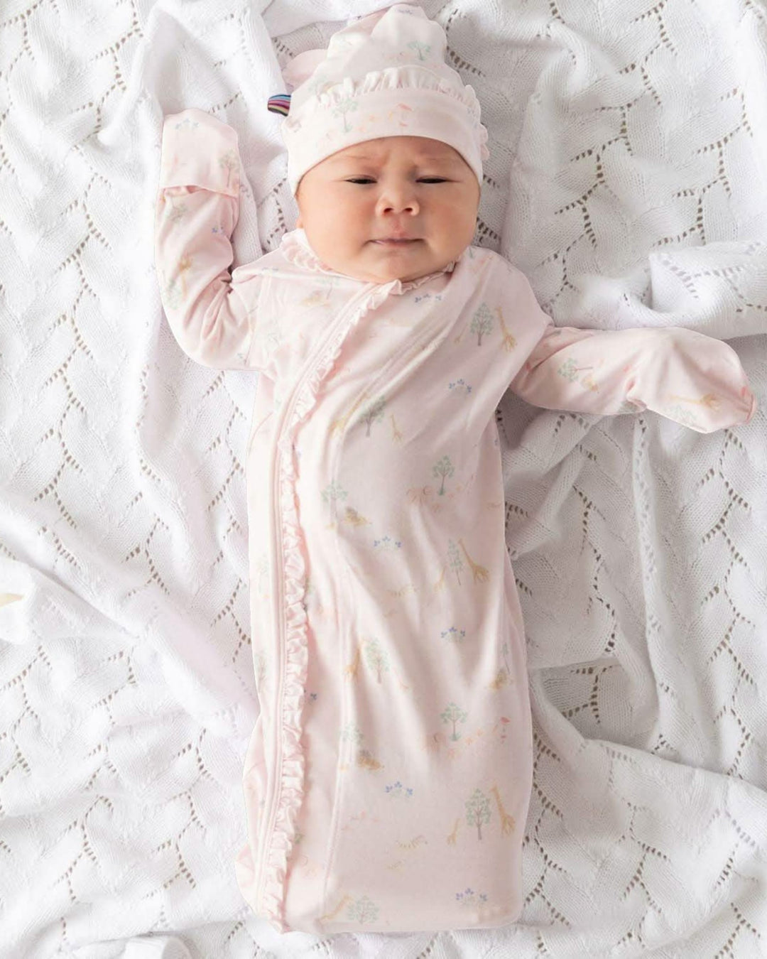 Baby wrapped in a pink swaddle with a matching hat on a white textured blanket