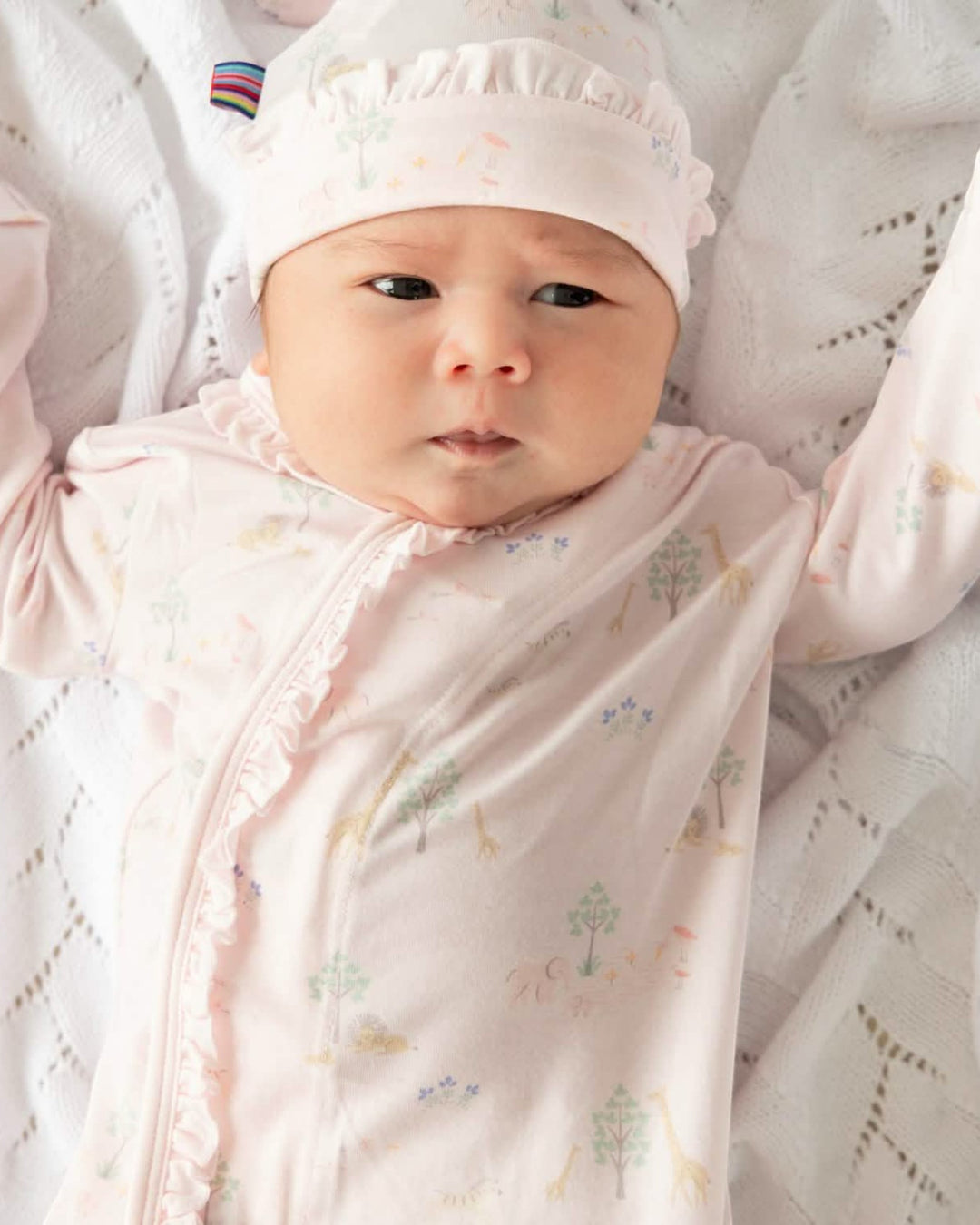 Newborn baby wrapped in a pink blanket with a white hat, lying on a textured surface.