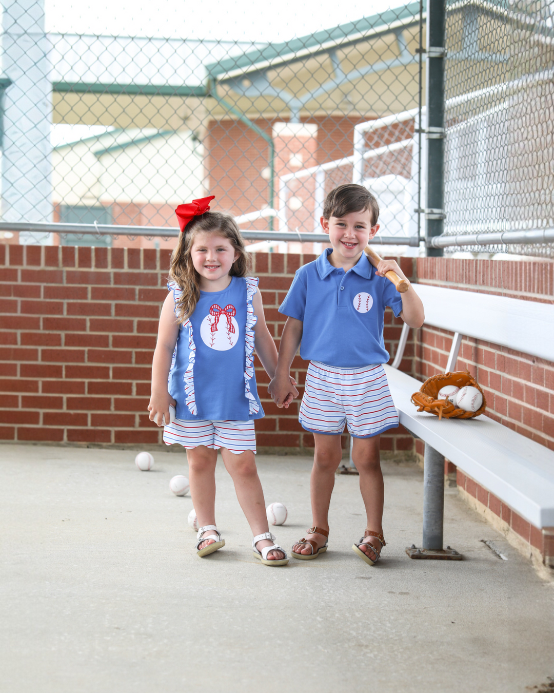 Two children in matching blue outfits standing on a baseball field.