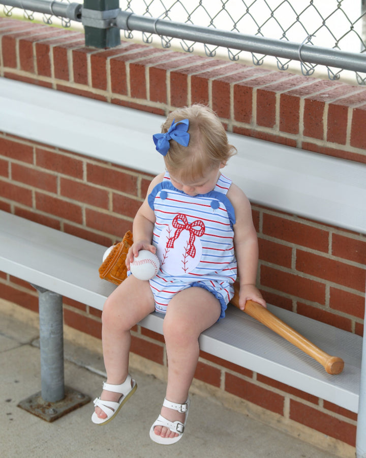 Child sitting on a bench with sports equipment, wearing a red, white, and blue outfit.