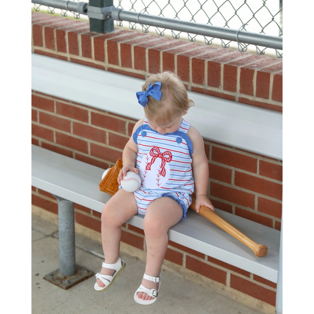 Child sitting on a bench with sports equipment, wearing a red, white, and blue outfit.