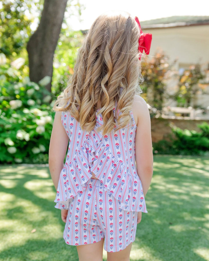 Child wearing a floral dress with a red bow in a garden setting, that store
