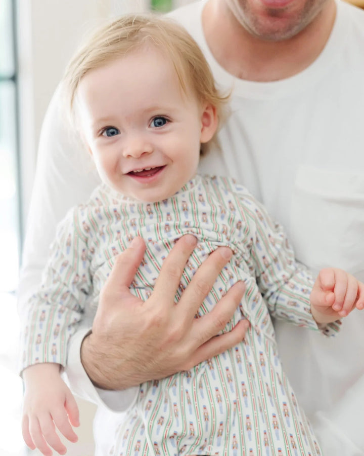 Baby in a patterned outfit being held by an adult indoors