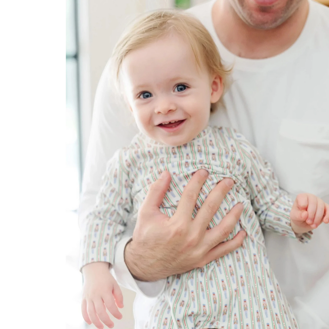Baby in a patterned outfit being held by an adult indoors