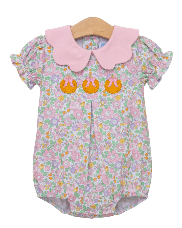 A baby romper with a light pink floral print, featuring a solid light pink Peter Pan collar and three orange Easter egg appliqués on the chest, displayed on a wooden hanger against a white background, that store