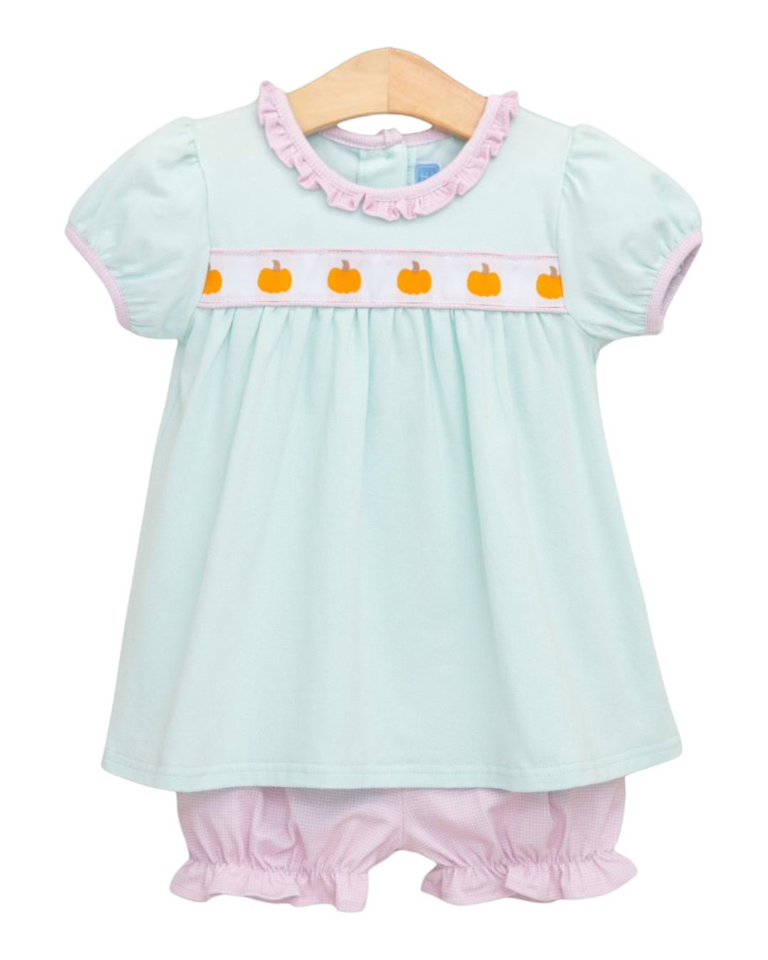 A baby girl's two-piece outfit consisting of a mint green smocked dress with a pink ruffled collar and yellow pumpkin trim, paired with light pink ruffled bloomers, hanging on a wooden hanger against a white background, that store