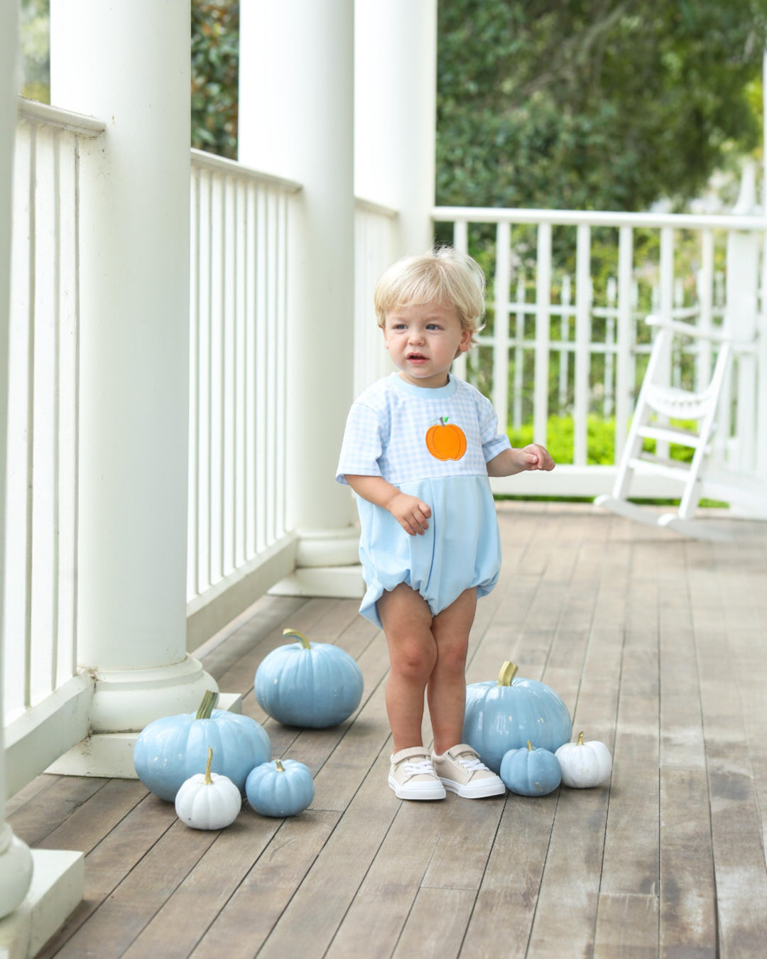 Child standing on a wooden deck with blue pumpkins
