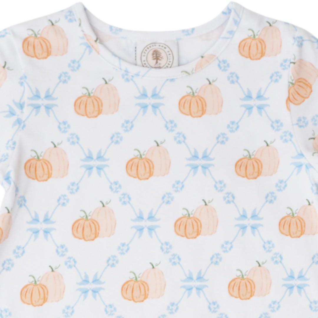 A close-up of a white long-sleeve top featuring a repeating pattern of orange and peach watercolor pumpkins and light blue floral starburst motifs, that store
