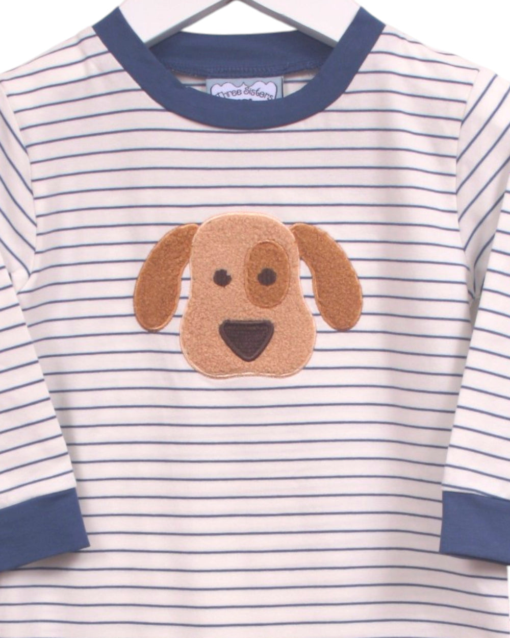 A children's long-sleeve top with navy blue and white horizontal stripes, featuring a brown dog face applique on the chest and navy blue ribbed collar and cuffs. A heart-shaped brand label is visible inside the collar, that store