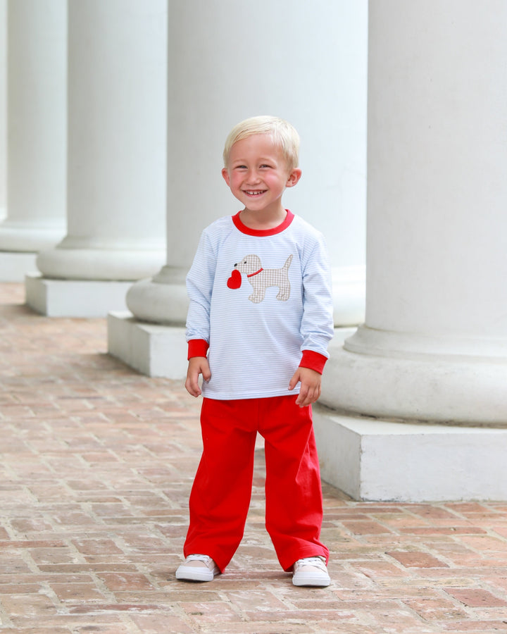 Child wearing a white and red outfit with a dog graphic in front of classical columns.