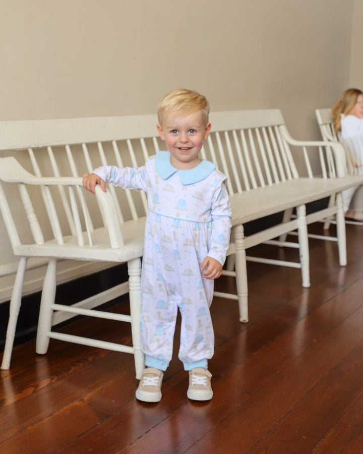 Young boy in a light blue pajama set standing in a room with white benches.