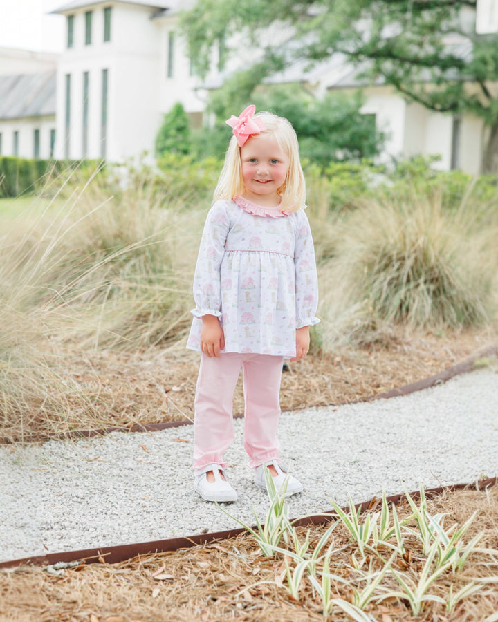 Young girl in a pink outfit standing outdoors with grass and a house in the background