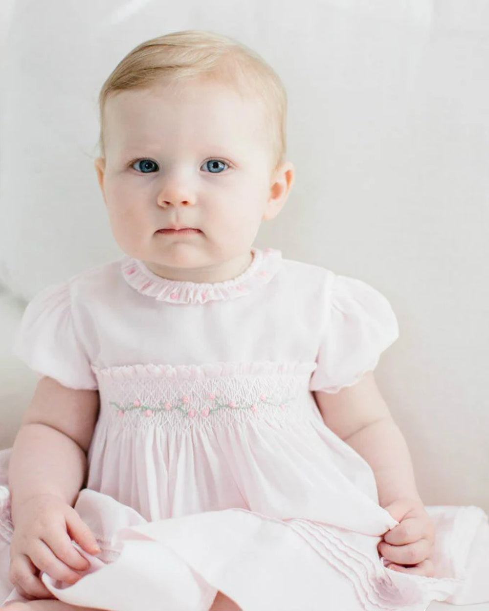 Baby in a pink dress with ruffled collar and sleeves against a light background