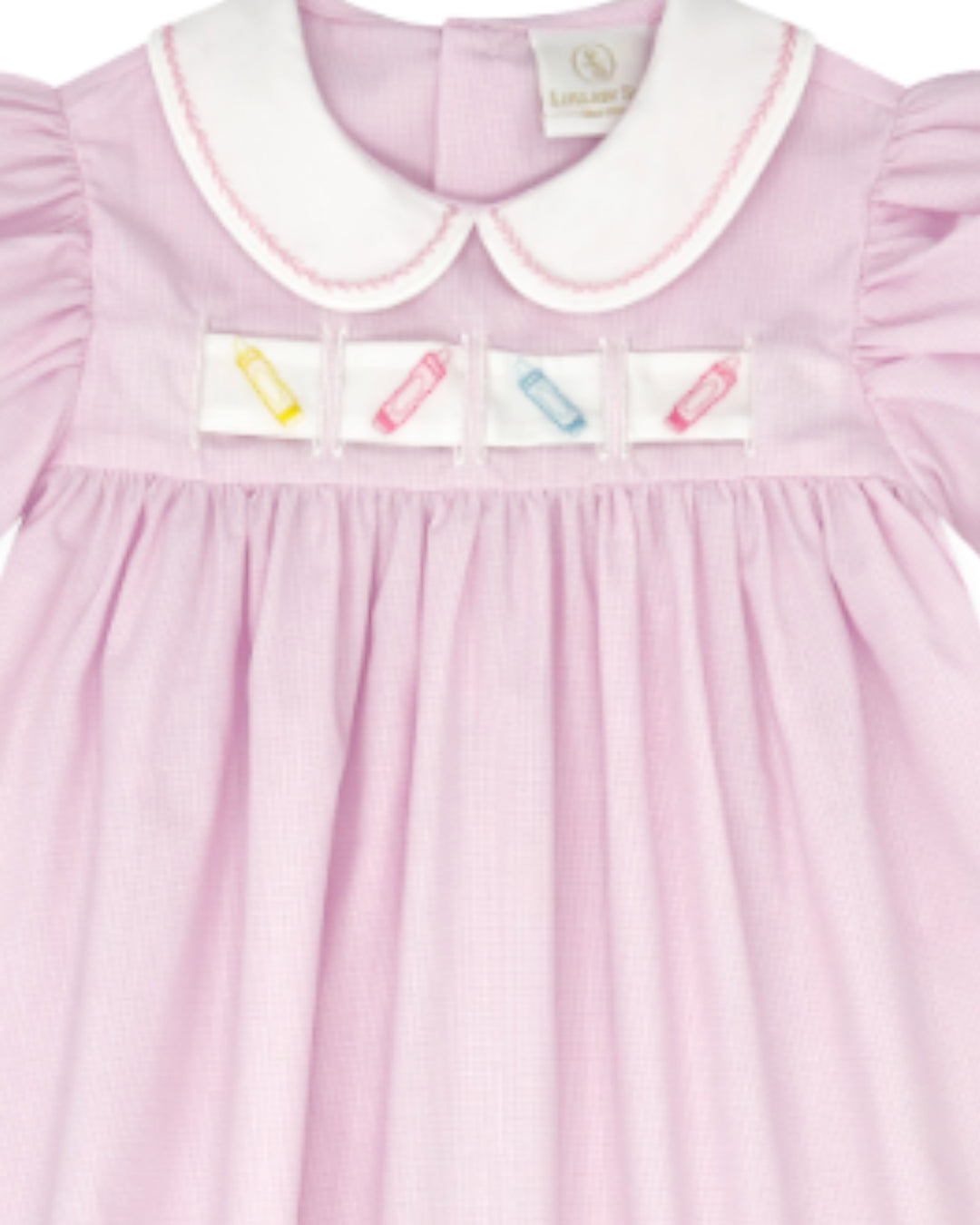 A close-up of a light pink gingham baby dress with a white Peter Pan collar, featuring four small colorful embroidered pencil patches across the chest, that store
