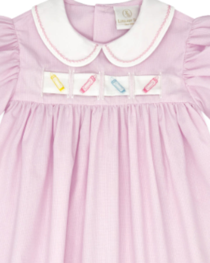 A close-up of a light pink gingham baby dress with a white Peter Pan collar, featuring four small colorful embroidered pencil patches across the chest, that store