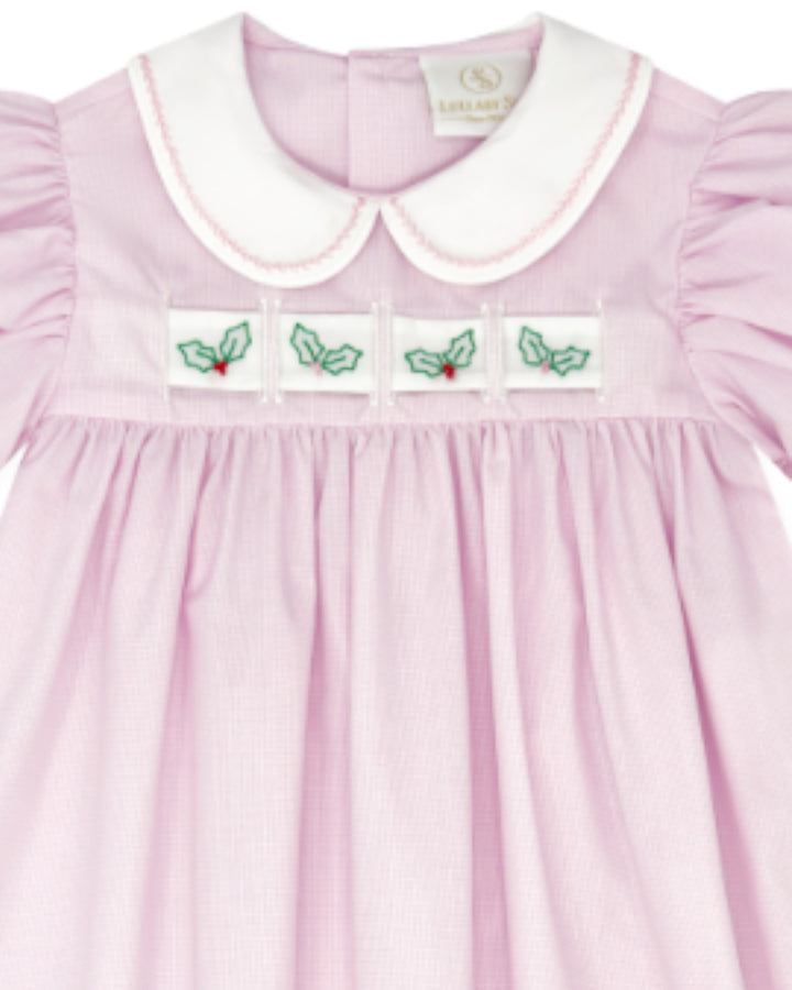 A close-up of a light pink baby dress with a white Peter Pan collar, featuring four embroidered holly motifs across the chest, that store
