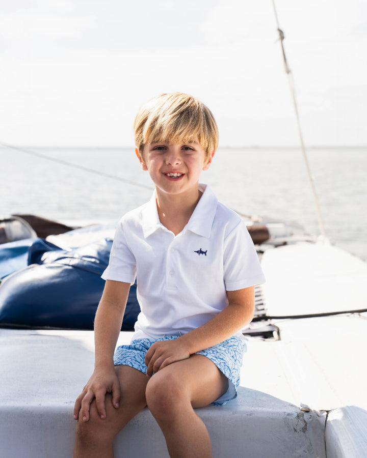Young boy in a white polo shirt and light blue shorts sitting on a boat.