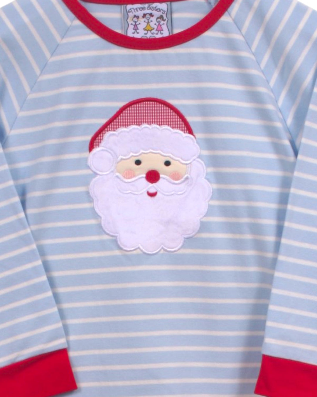 A close-up of a baby long-sleeve shirt with light blue and white horizontal stripes, featuring a red crew neck, red cuffs, and a white embroidered Santa Claus face patch on the chest, that store
