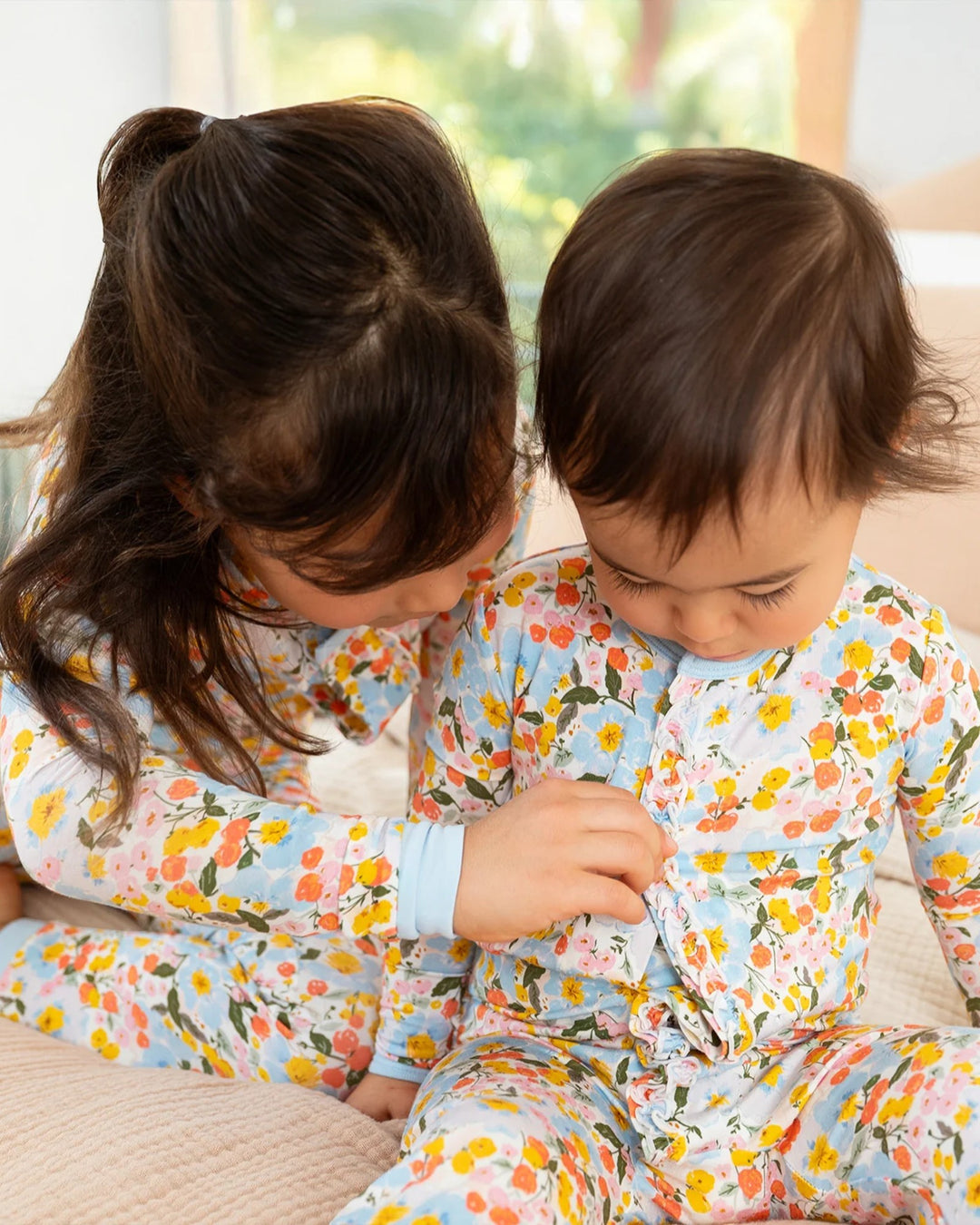 Two children wearing floral pajamas sitting on a couch.