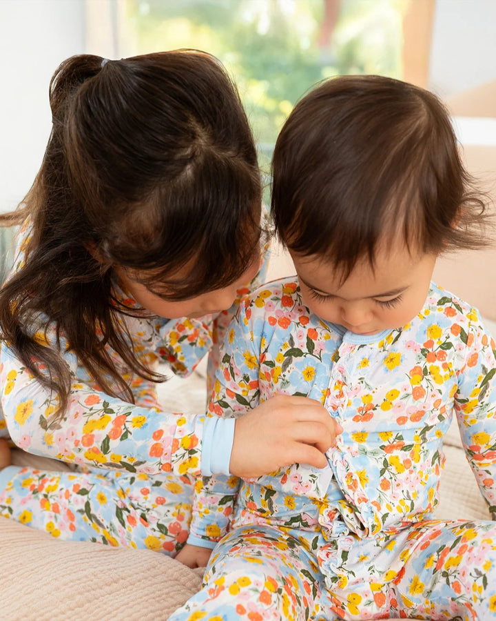 Two children wearing floral pajamas sitting on a couch.