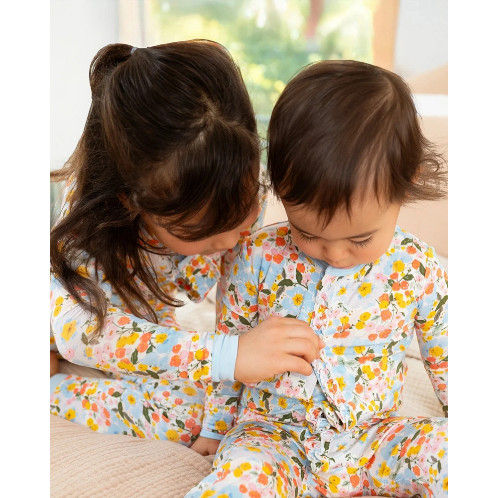 Two children wearing floral pajamas sitting on a couch.