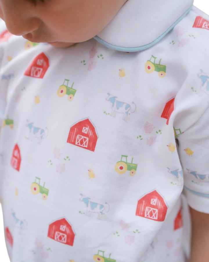 Close-up of a baby wearing a white short-sleeve bodysuit with a colorful farm print featuring red barns, green tractors, and light blue cows, that store