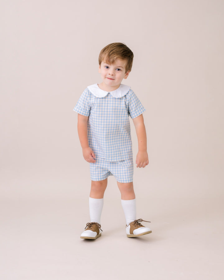 Child wearing a checkered outfit with a collar on a beige background