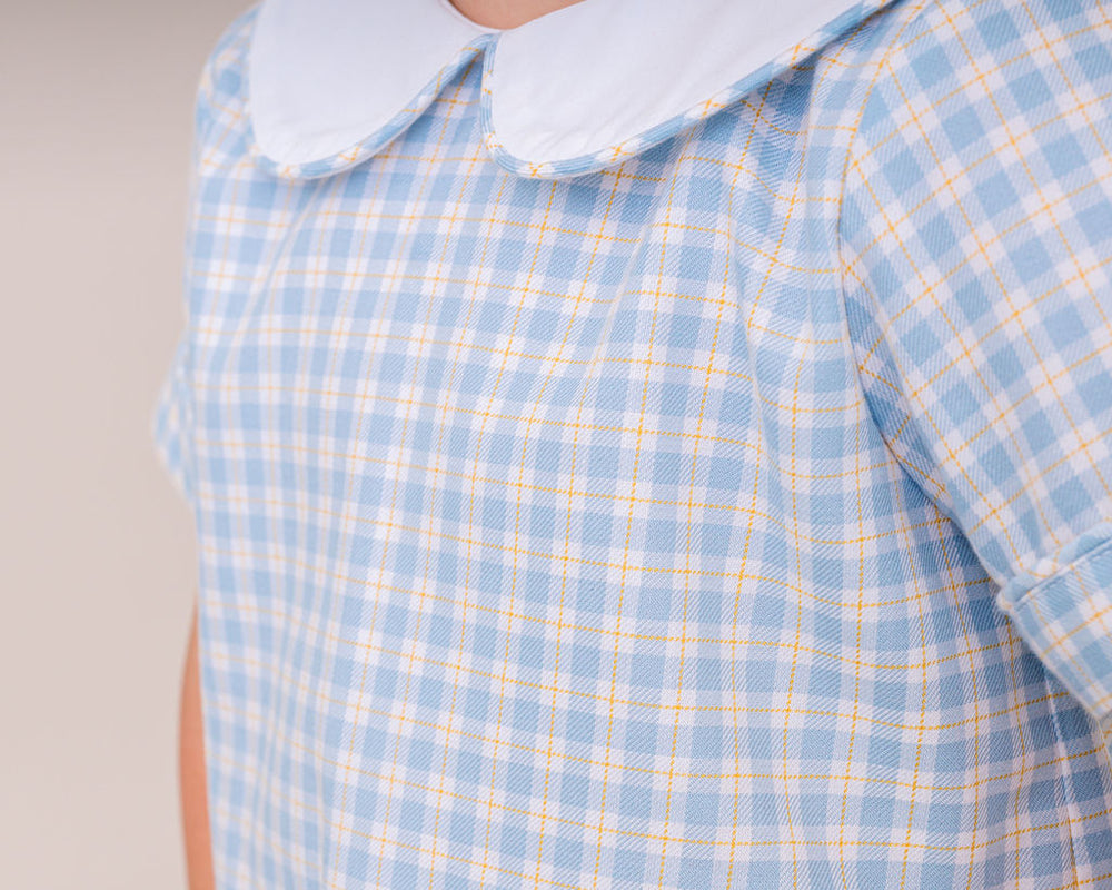 Blue and yellow checkered shirt with a white collar on a neutral background