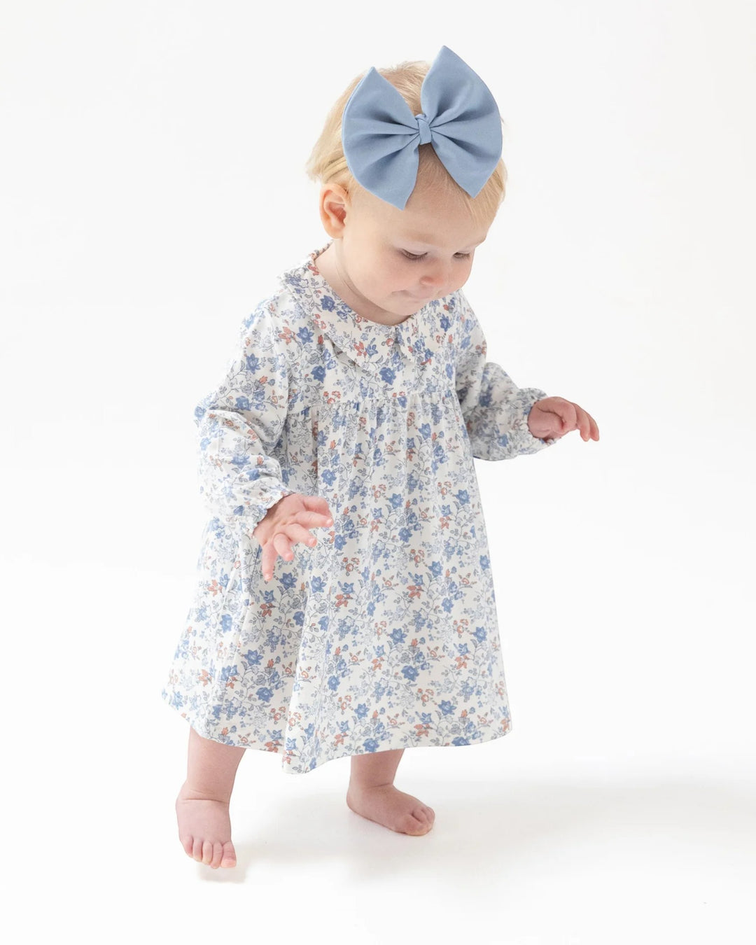 Baby wearing a floral dress and blue headband on a white background