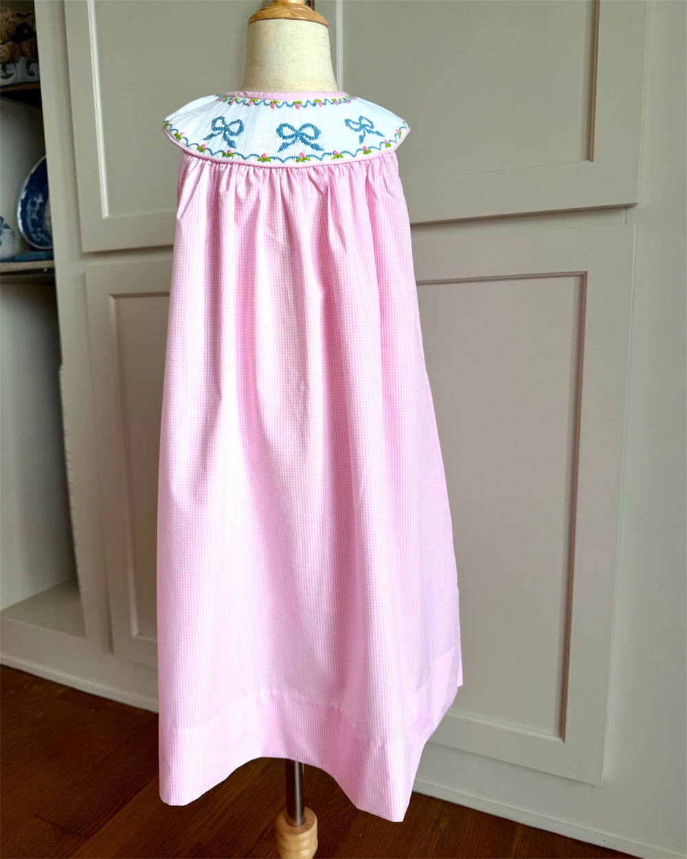 Pink dress with embroidered collar on a mannequin against a white cabinet background