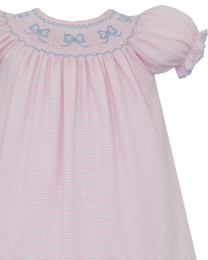 A close-up of a baby dress with light pink and white vertical stripes, featuring smocked bodice with blue bow details and ruffled short sleeves, that store