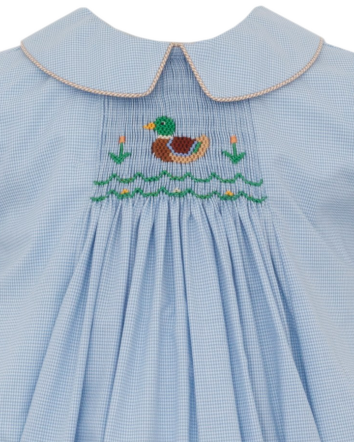 A close-up of a light blue gingham dress featuring a smocked bodice with an embroidered mallard duck and reeds, finished with a Peter Pan collar, that store