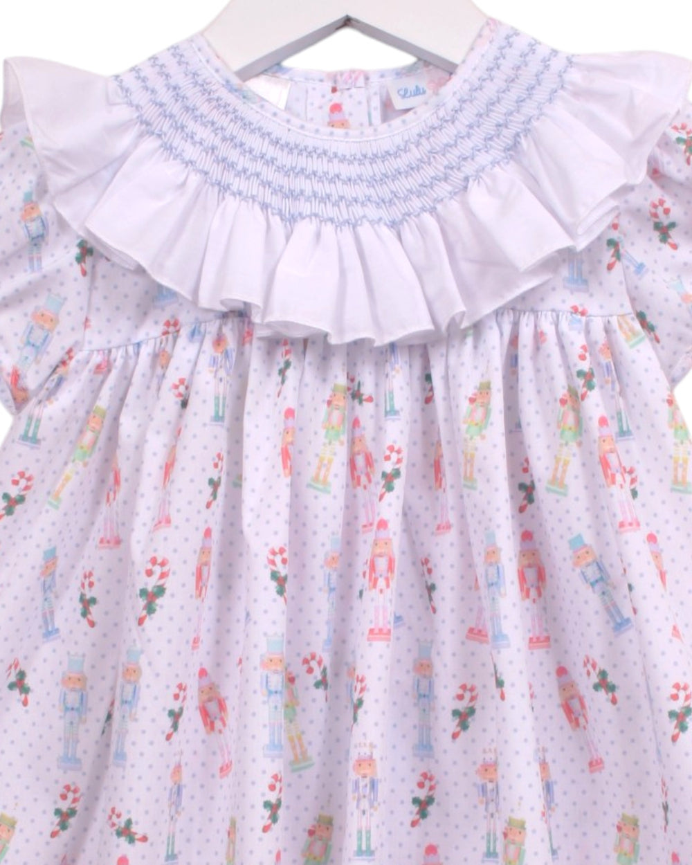A baby girl's smocked dress with a white base, light blue smocked collar, and a colorful nutcracker pattern with tiny polka dots, that store