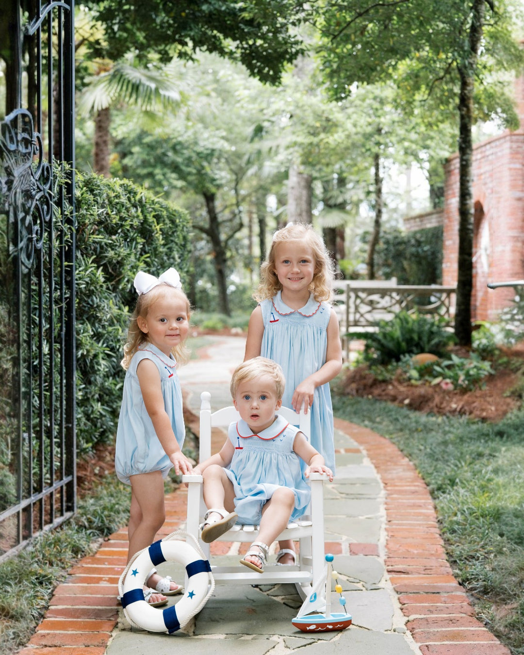 Three young children in matching dresses sitting on a bench outdoors.