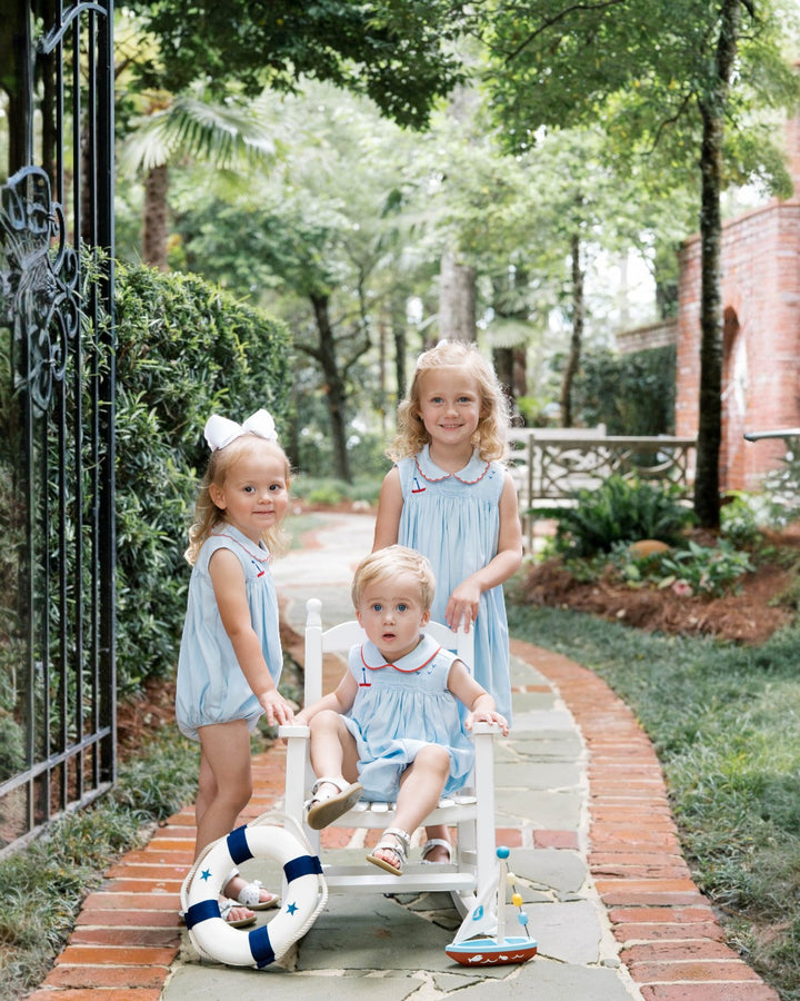 Three young children in matching dresses sitting on a bench outdoors.