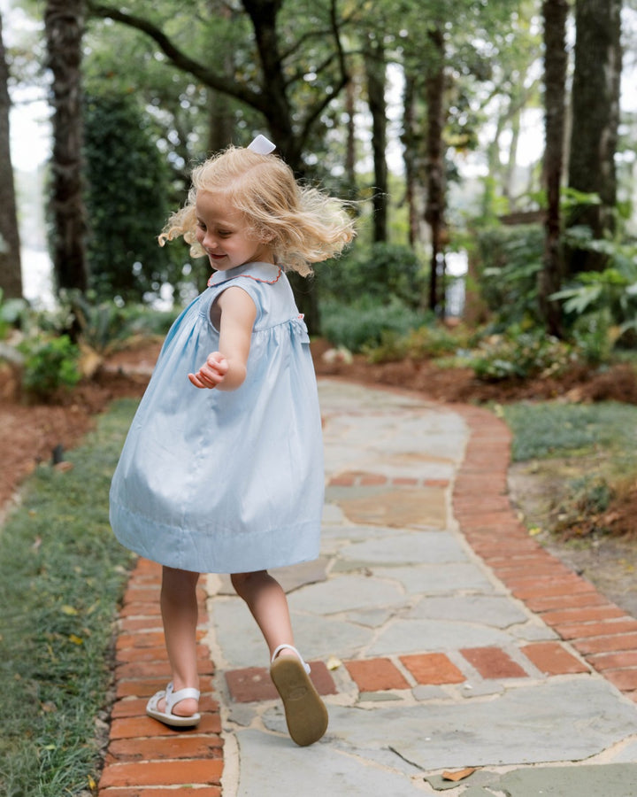 Child in a light blue dress walking on a stone path in a garden.