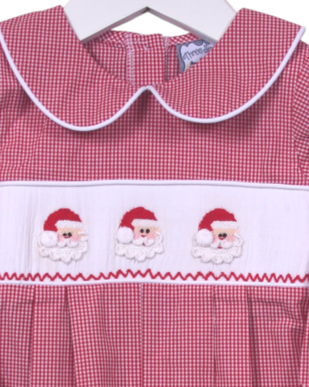 Red gingham dress with embroidered Santa faces on a hanger