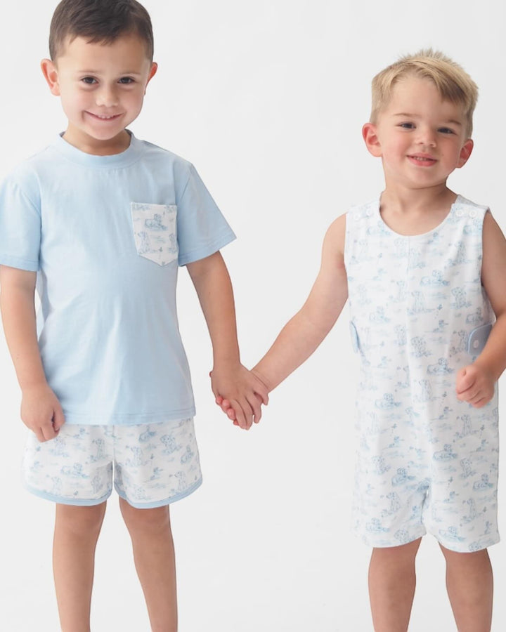 Two young boys holding hands, wearing matching light blue outfits with subtle patterns on a white background.