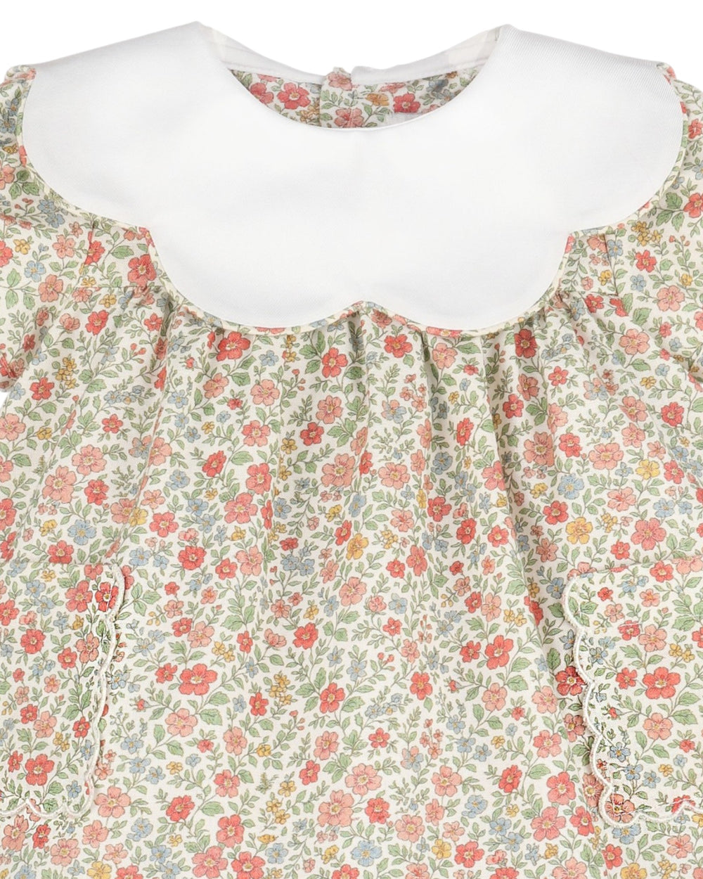 Close-up of a children's dress with a white scalloped Peter Pan collar and a dense small floral print in coral, green, and muted blue on an off-white background, that store