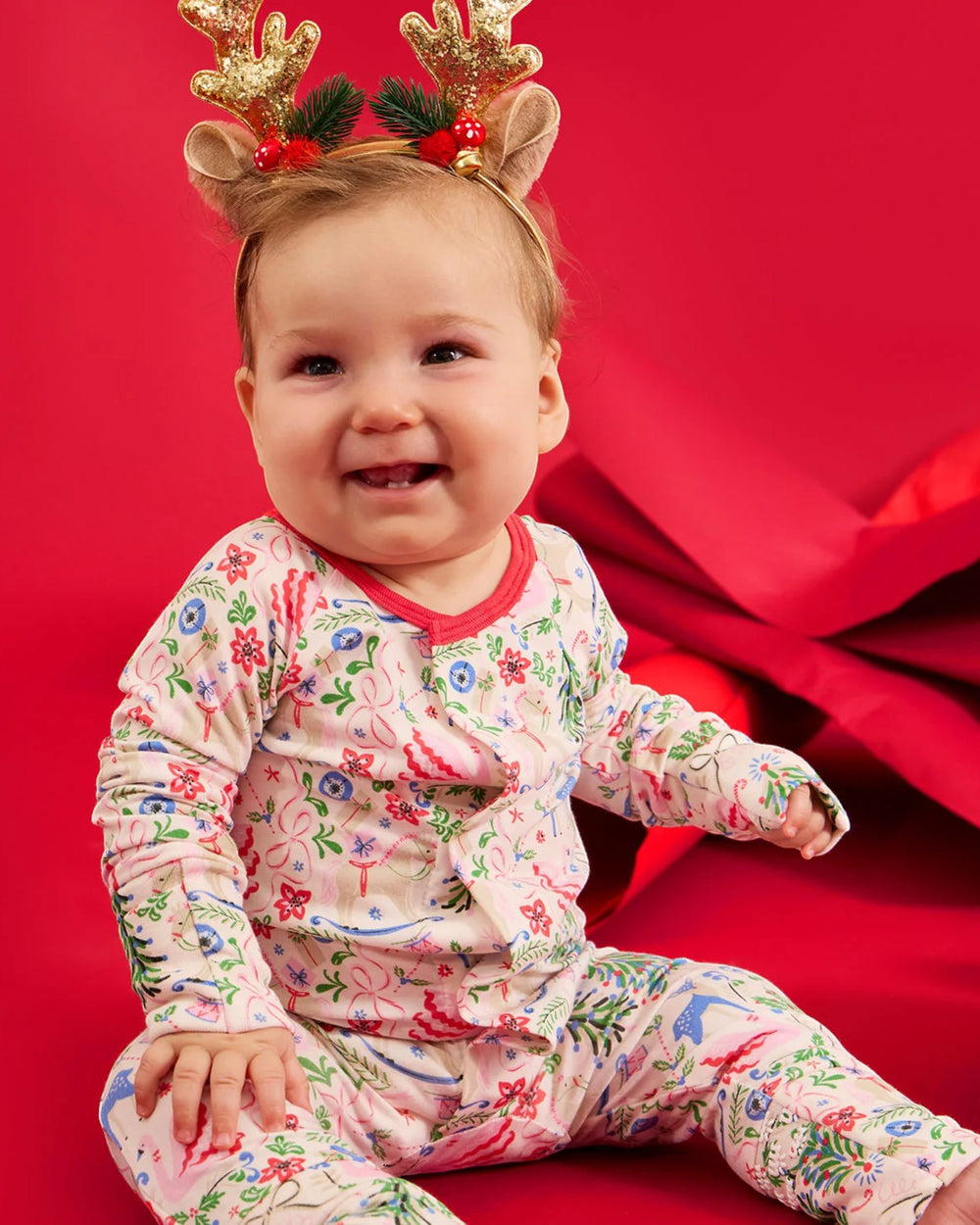 Baby wearing a floral outfit and reindeer antlers on a red background