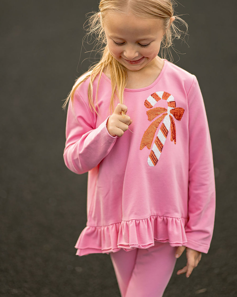 Young girl wearing a pink outfit with a candy cane design on a dark background