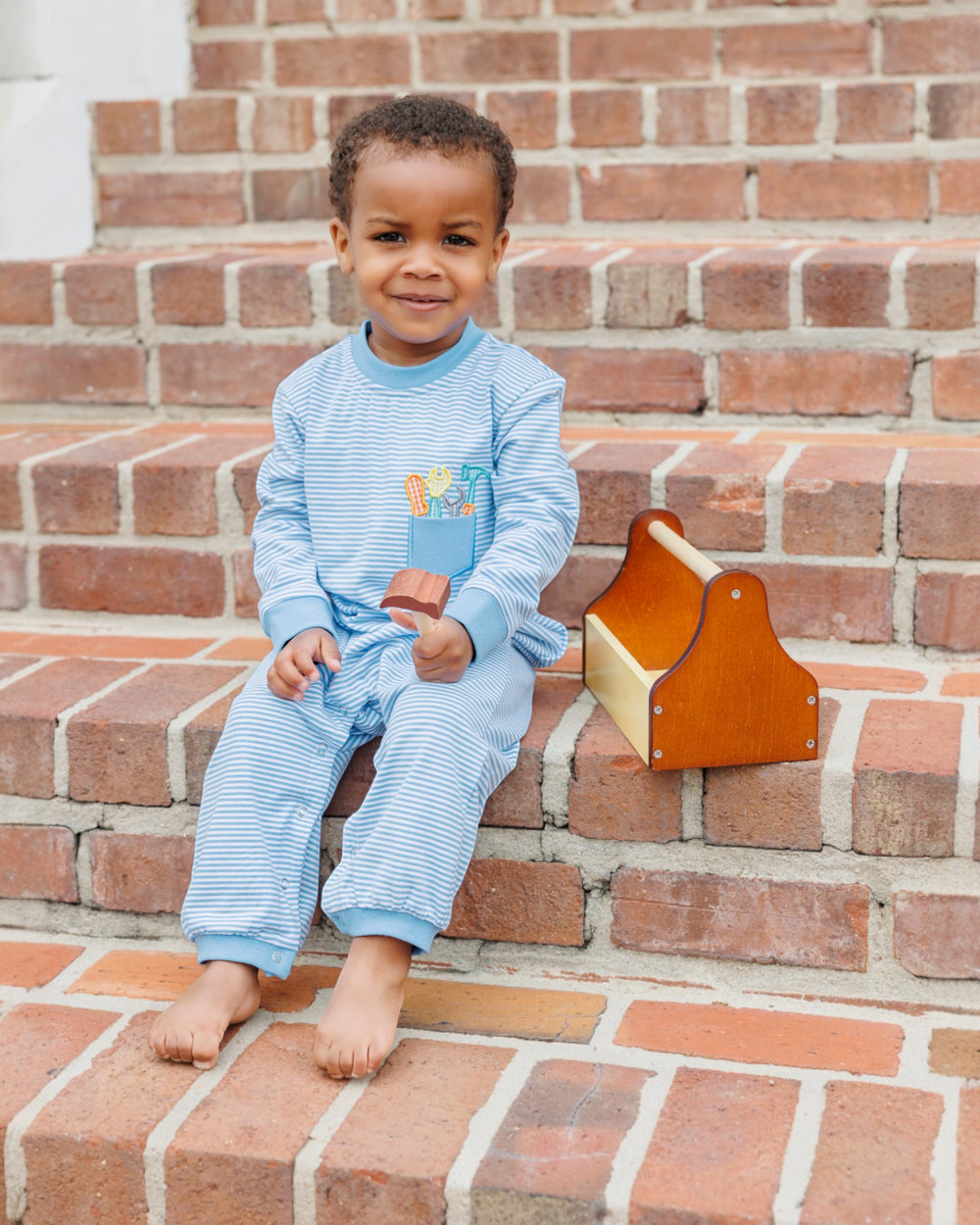 Child in blue pajamas sitting on brick steps with a wooden toy.